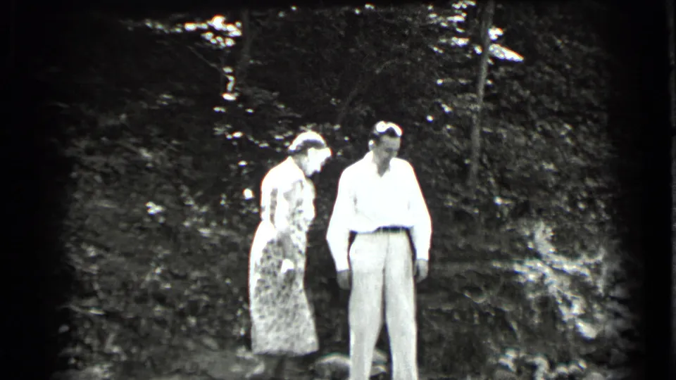 Two women in late-1930s-style dresses stand together near the wooded creek at Clear Lake, California.