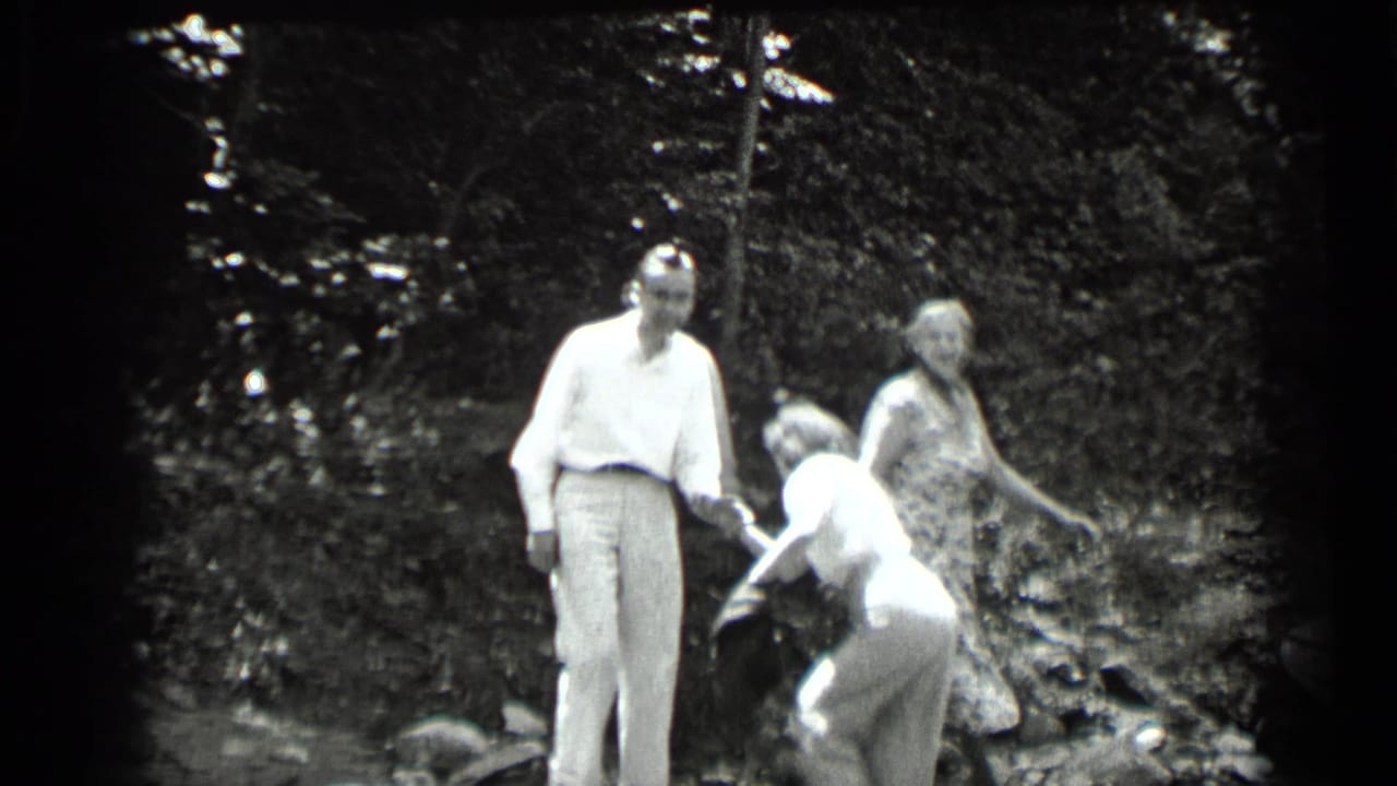 Three adults standing and bending near trees in an outdoor wooded area.