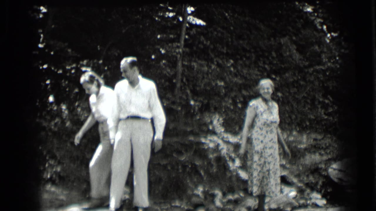 Three adults walking and standing near a wooded creek or lakeside edge.