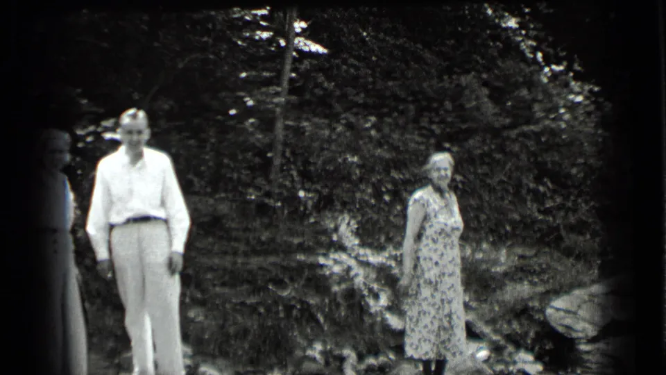 1939 Clear Lake frame with a man in light clothing and a woman in a patterned dress standing apart in a wooded setting.