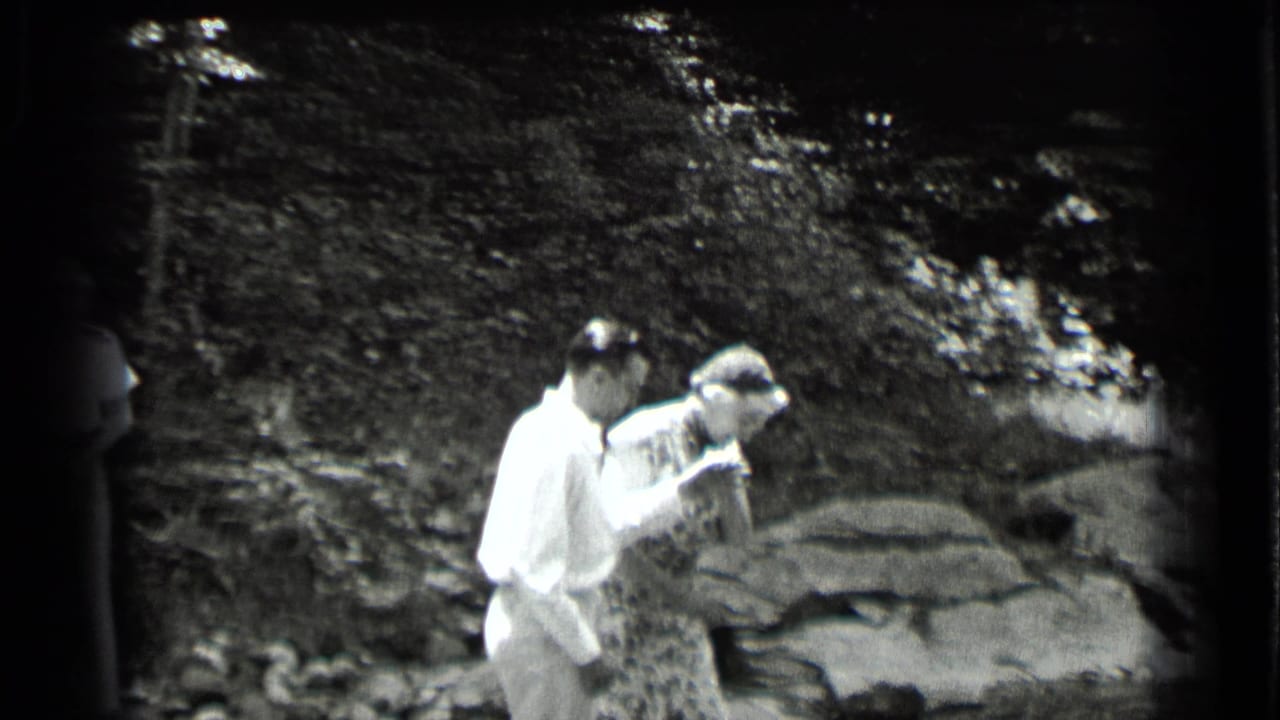 Man holds a woman's arm as she steps near rocks and water.