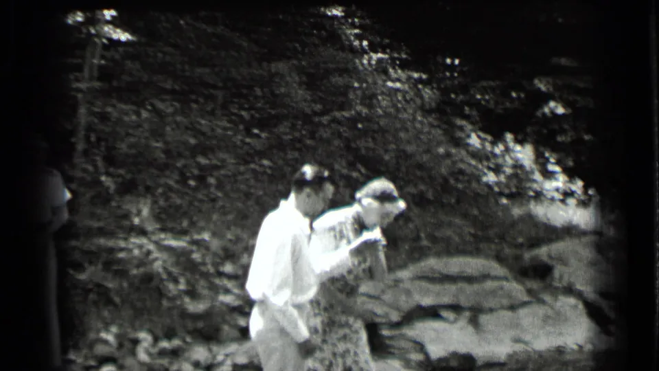 The man assists the woman in a patterned dress as she begins crossing the rocky stream area at Clear Lake in 1939.