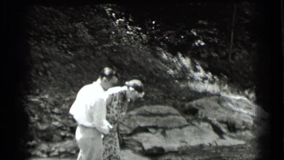 In the 1939 Clear Lake home movie, the man keeps close behind the woman as she leans forward over rocks beside the stream.