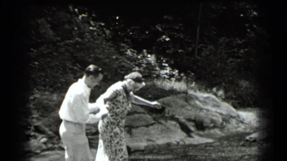 The woman steps across the shallow stream while the man follows closely behind on the rocky bank in Clear Lake, California.