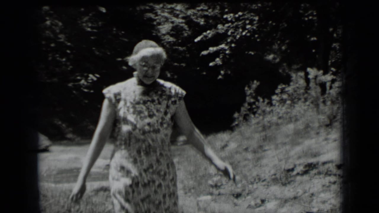 Adult woman in a floral dress walks through a shaded Clear Lake, California forest in 1939 home-movie footage.