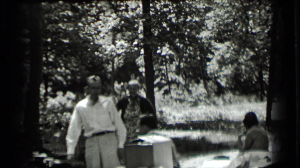 In Clear Lake, California home-movie footage from 1939, adults stand and sit near tables under trees in dappled sunlight.