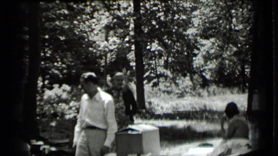 A man in light trousers stands by an outdoor table while other adults remain nearby in the 1939 Clear Lake park scene.