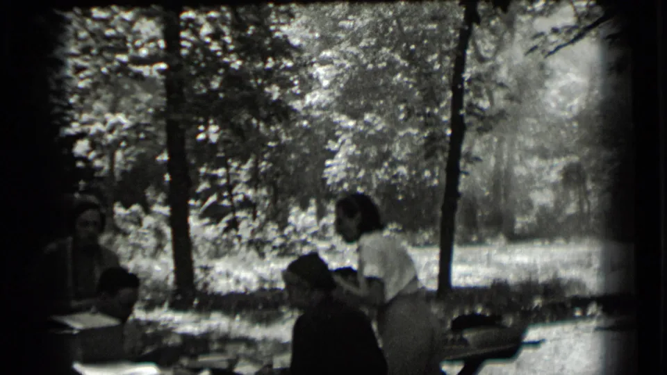 The group remains around the shaded outdoor table in the Clear Lake home movie, with faces partly visible in soft focus.