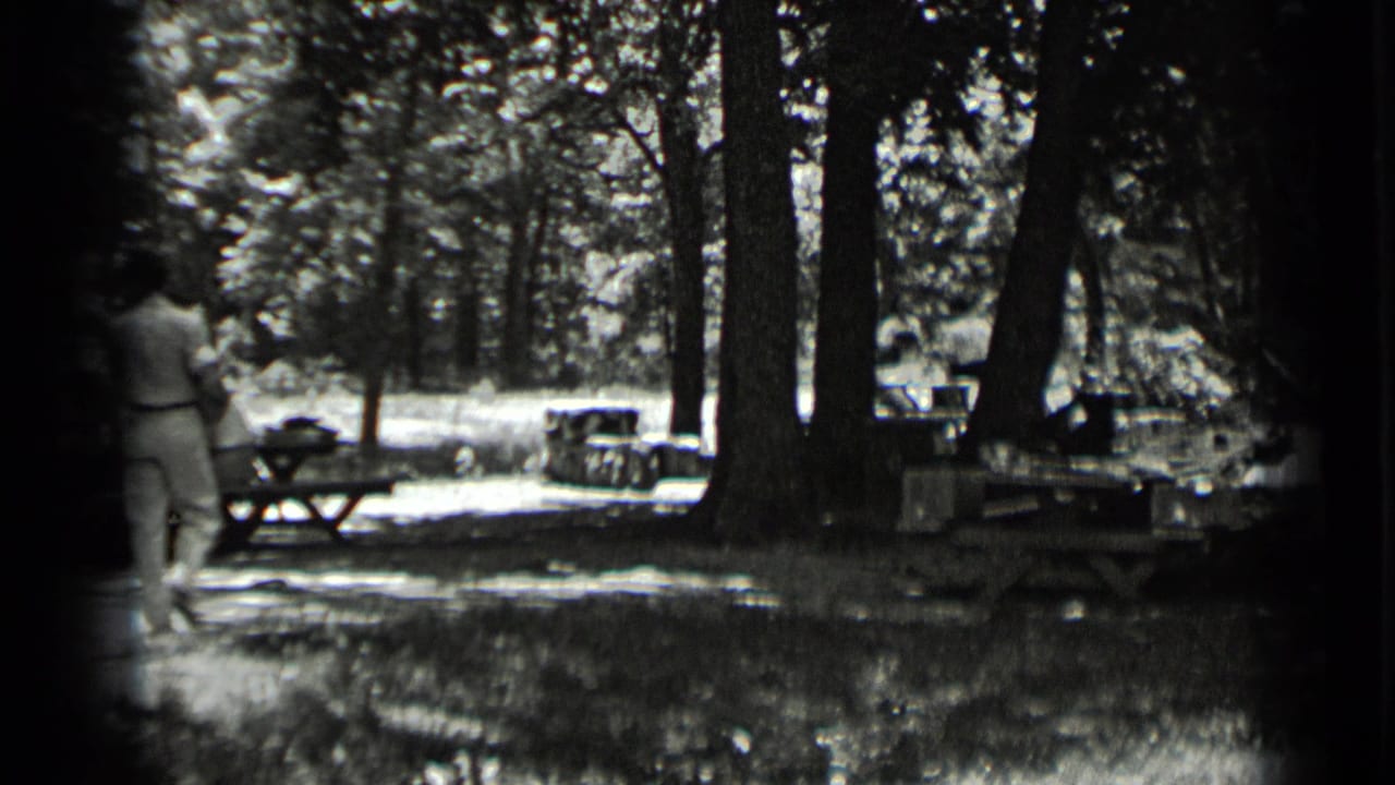 In 1939 Clear Lake home-movie footage, adults walk away through a shaded wooded picnic area with tables and bright sun patches.