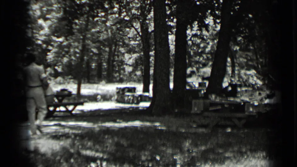 In 1939 Clear Lake home-movie footage, adults walk away through a shaded wooded picnic area with tables and bright sun patches.