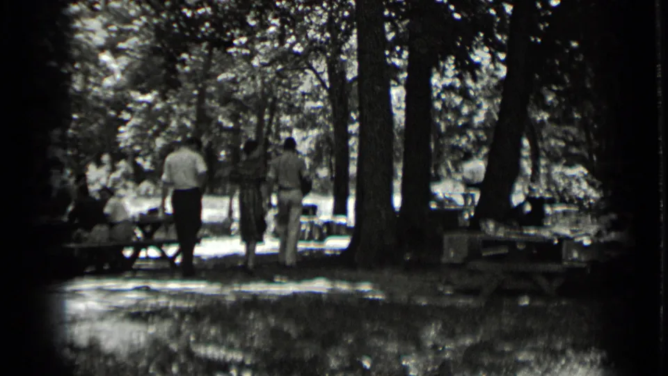 The group recedes into the wooded Clear Lake picnic area, framed by trees, sunlit ground, and soft 8mm film grain.