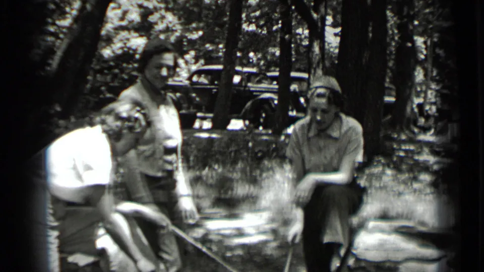At Clear Lake in 1939, three women gather by a small campfire with roasting sticks and a parked car visible through the trees.