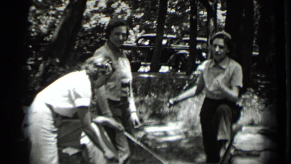 Three women in period clothing tend roasting sticks over a small campfire at a wooded Clear Lake outing in 1939.