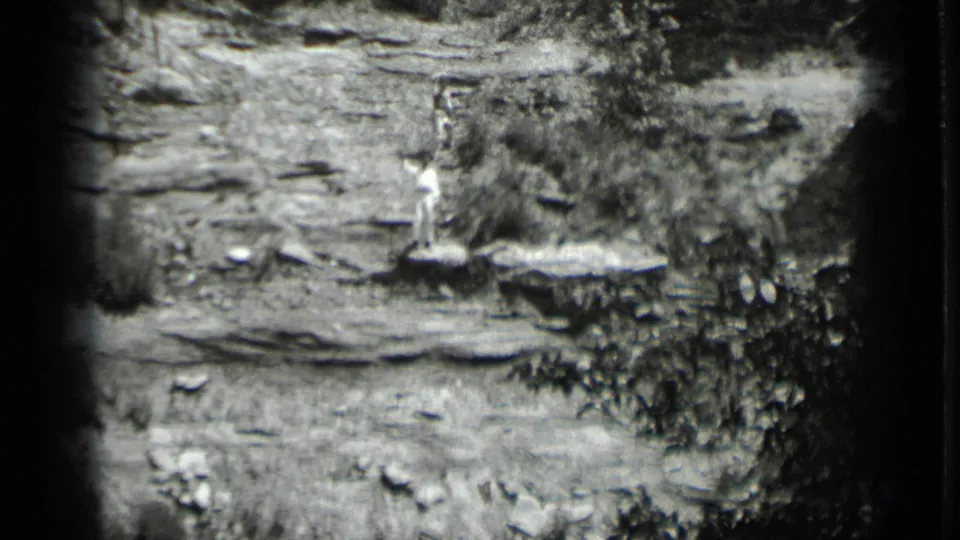 1939 Clear Lake, California home-movie frame showing a lone person waving from a rocky ledge in a rugged black-and-white landscape.