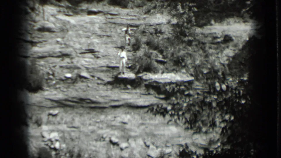 Distant figure at Clear Lake appears to wave from a rocky outcrop, framed by dark 8mm edges and sparse vegetation.