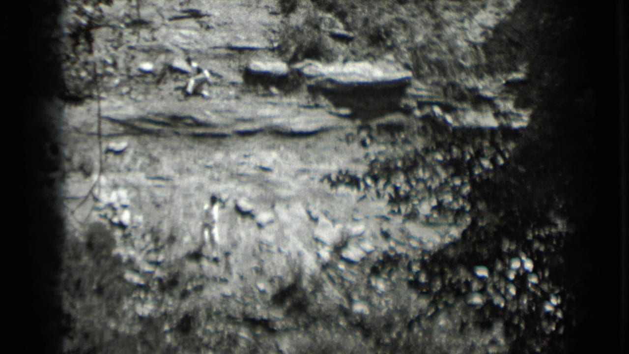 1939 Clear Lake home-movie frame showing rocky terrain, brush, and a distant figure in light clothing on a steep outdoor slope.