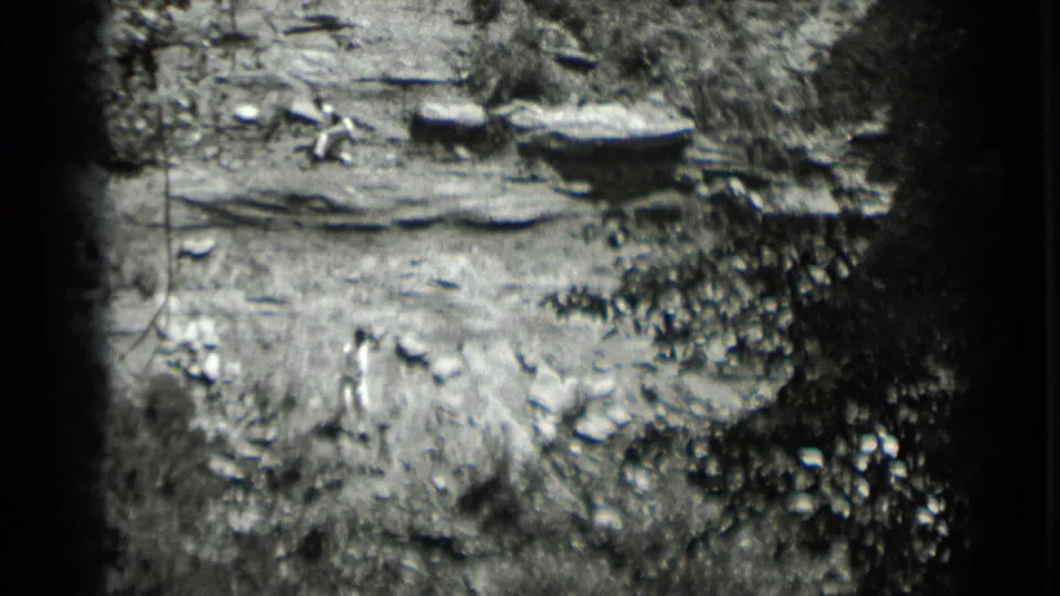 1939 Clear Lake home-movie frame showing rocky terrain, brush, and a distant figure in light clothing on a steep outdoor slope.