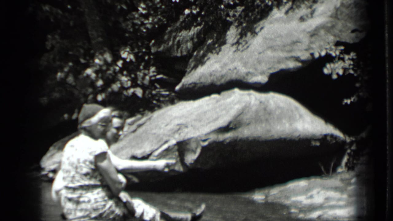 Two women share a quiet moment beside shallow water at Clear Lake, California, with boulders and trees filling the frame.