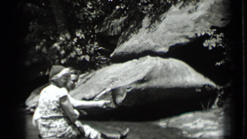 Two women share a quiet moment beside shallow water at Clear Lake, California, with boulders and trees filling the frame.