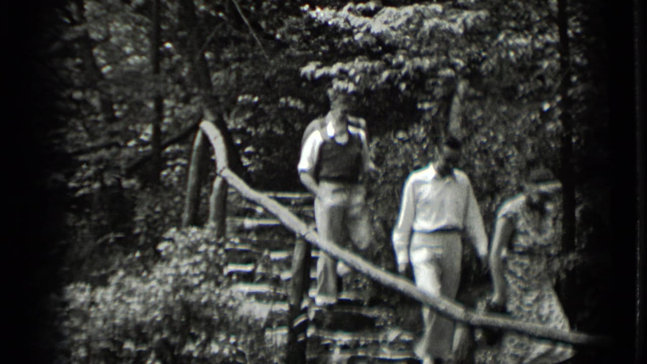 A closer home-movie view shows three adults on the wooded stone steps, with the railing cutting diagonally across the frame.