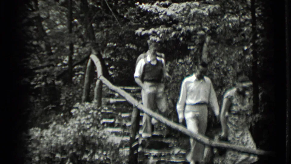 A closer home-movie view shows three adults on the wooded stone steps, with the railing cutting diagonally across the frame.
