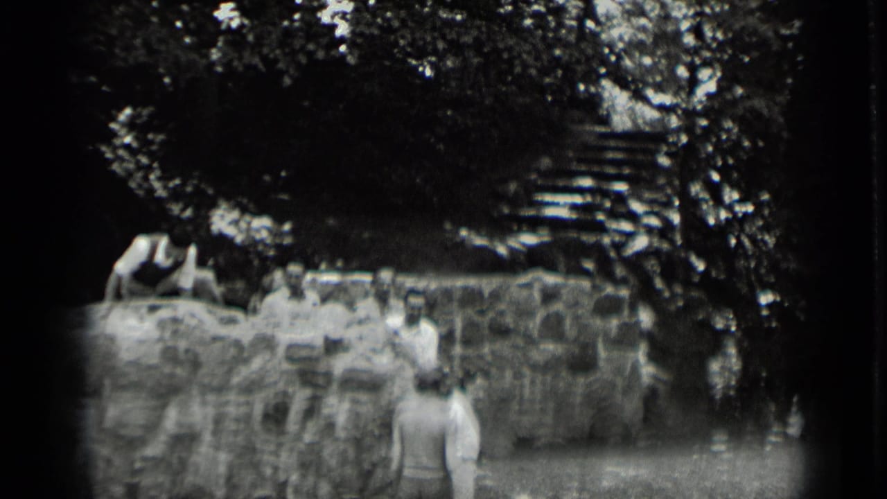 Adults gather around a rustic stone wall at Clear Lake, with one person seated above and steps visible through the trees.