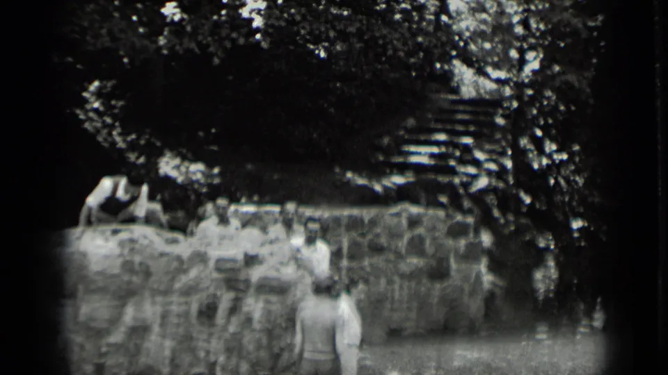 Adults gather around a rustic stone wall at Clear Lake, with one person seated above and steps visible through the trees.