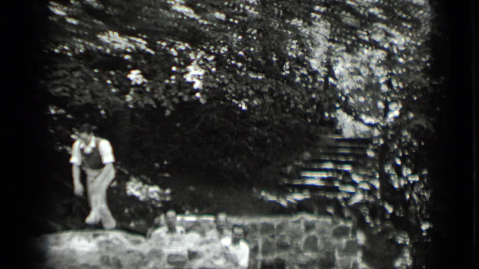 A man walks across the stone wall at Clear Lake while other adults sit or stand below in the wooded setting.