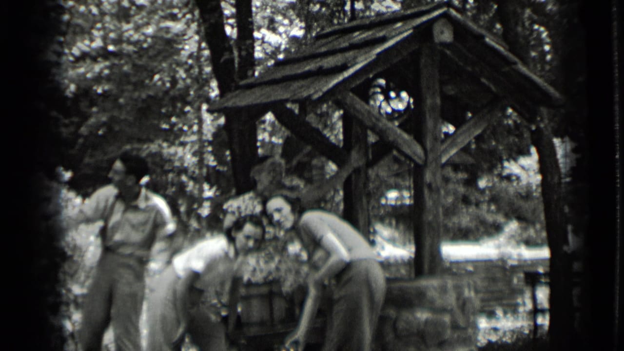 Young adults gather around a rustic wooden well in a wooded area.