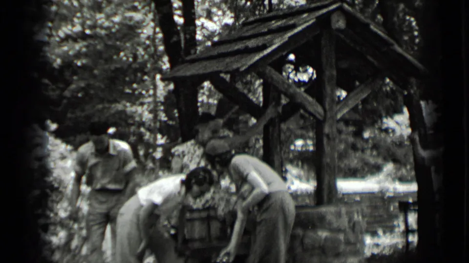 In Clear Lake, California, several young adults lean over a rustic well while one man stands to the side.