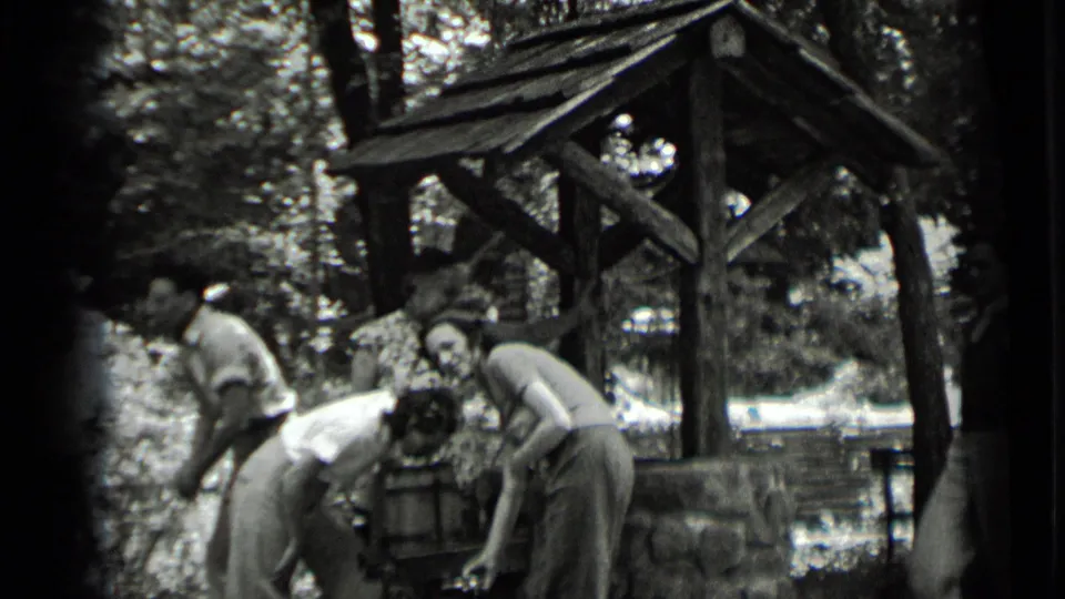 Young adults in 1939 Clear Lake footage bend close to the wooden well, partly obscured by soft 8mm exposure.