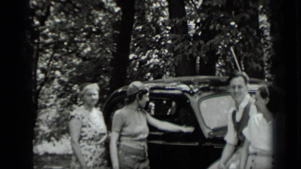 Adults at Clear Lake in 1939 stand beside a black car under trees, with one person leaning near the door and others facing the camera.