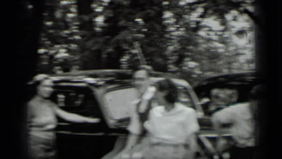Blurred 1939 home-movie frame of young adults near dark cars at Clear Lake, California, with trees in the background.
