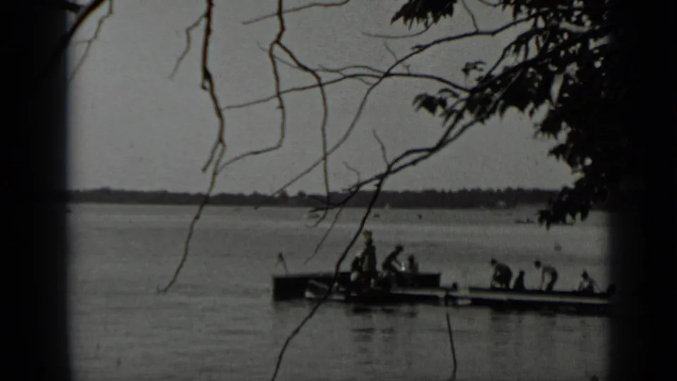 Clear Lake view with people gathered on a dock and small boat, seen through foreground branches in 1939 home-movie footage.
