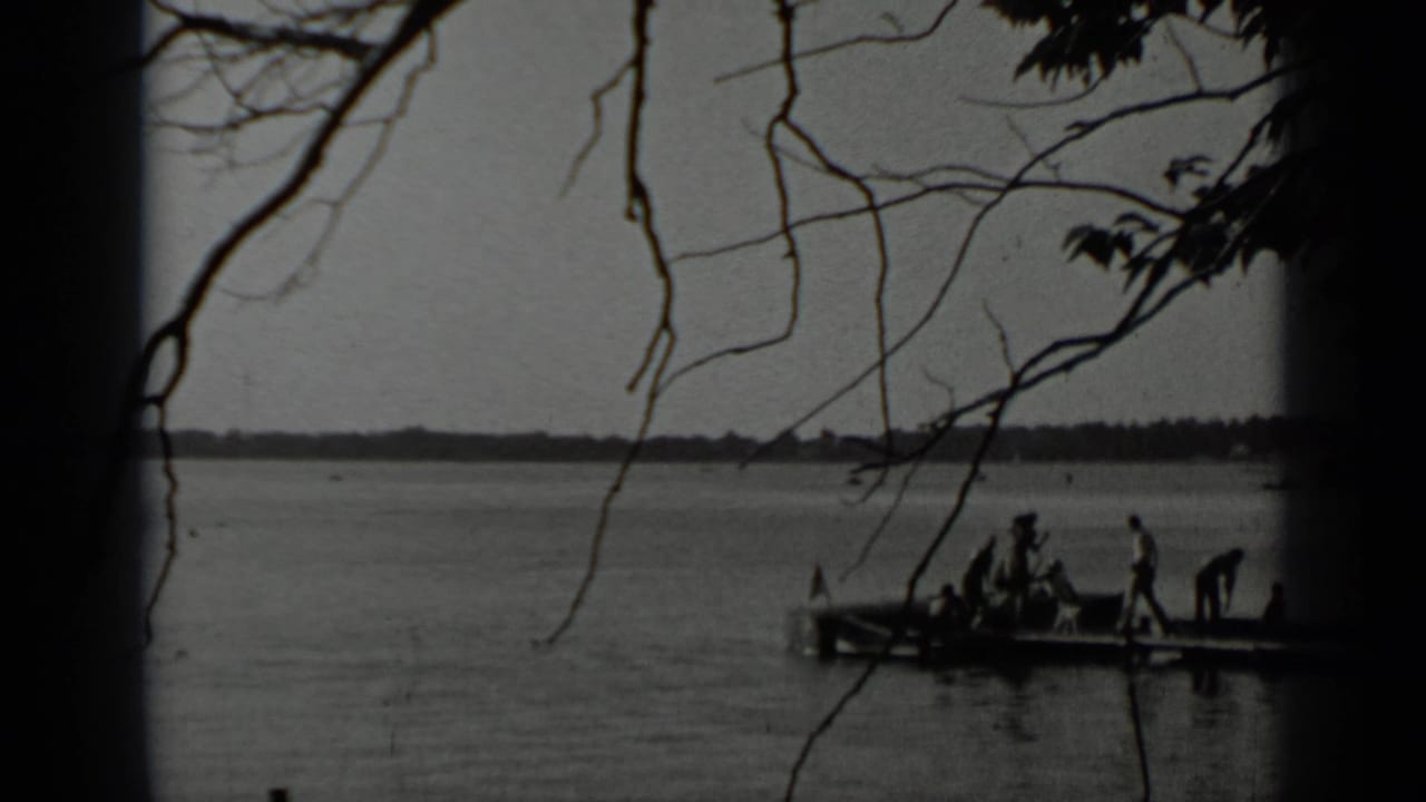 1939 Clear Lake home-movie frame with silhouetted people on a small wooden pier and bare branches across the view.