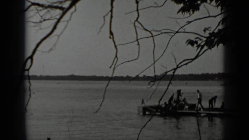1939 Clear Lake home-movie frame with silhouetted people on a small wooden pier and bare branches across the view.