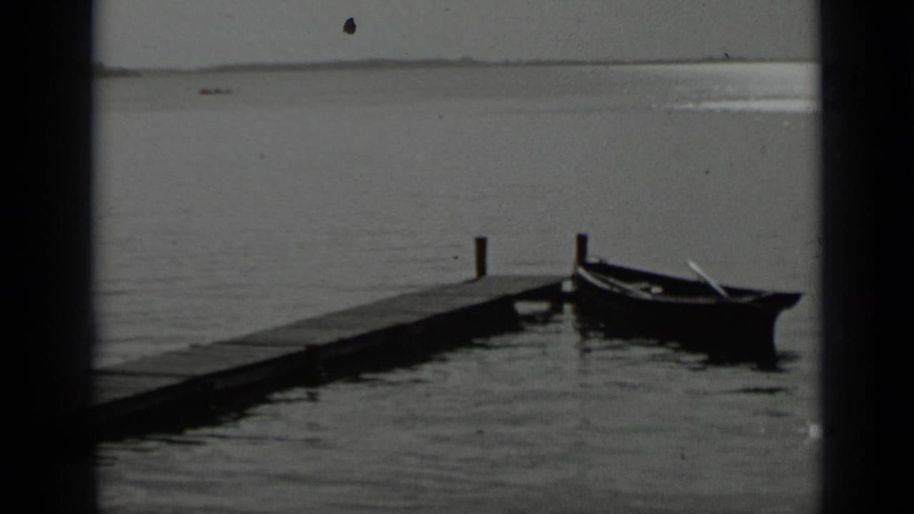 A rowboat rests beside a wooden pier extending into open lake water.