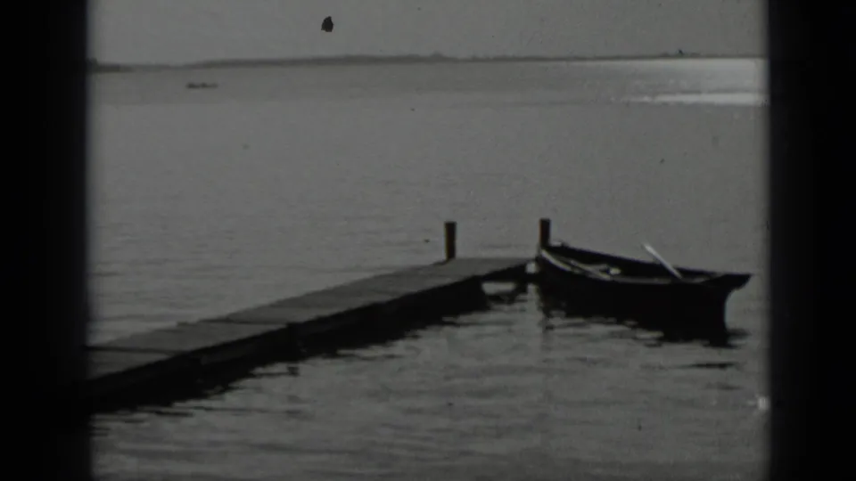 1939 Clear Lake view of a wooden pier with a small boat tied near its end and open water beyond.