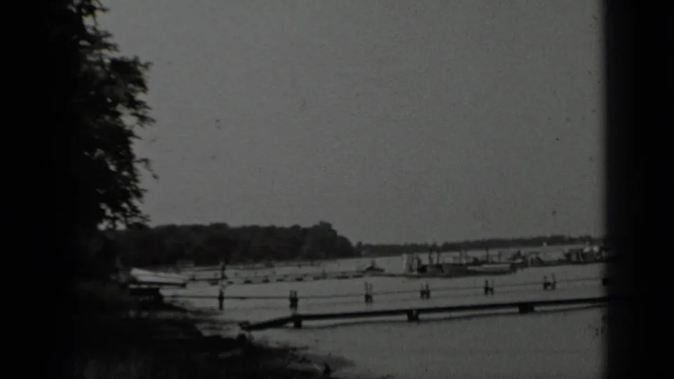 Wide 1939 Clear Lake frame showing multiple dock sections, small boats, calm water, and a tree-lined shore.