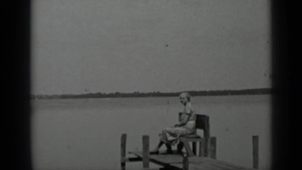 1939 Clear Lake home-movie frame showing an older woman in glasses seated on a wooden dock near calm water.