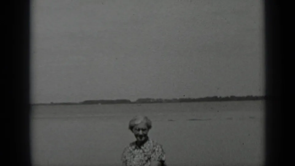 Black-and-white 8mm frame from Clear Lake showing the woman near the shore against a wide water horizon.