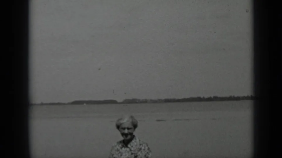 Clear Lake 1939 8mm frame showing an older woman smiling toward the camera with the shoreline in the distance.