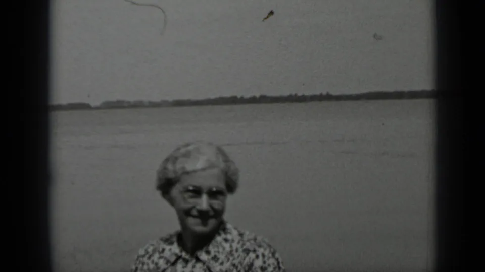 Older woman in glasses and patterned blouse smiles at the camera by Clear Lake, California, in 1939 home-movie footage.