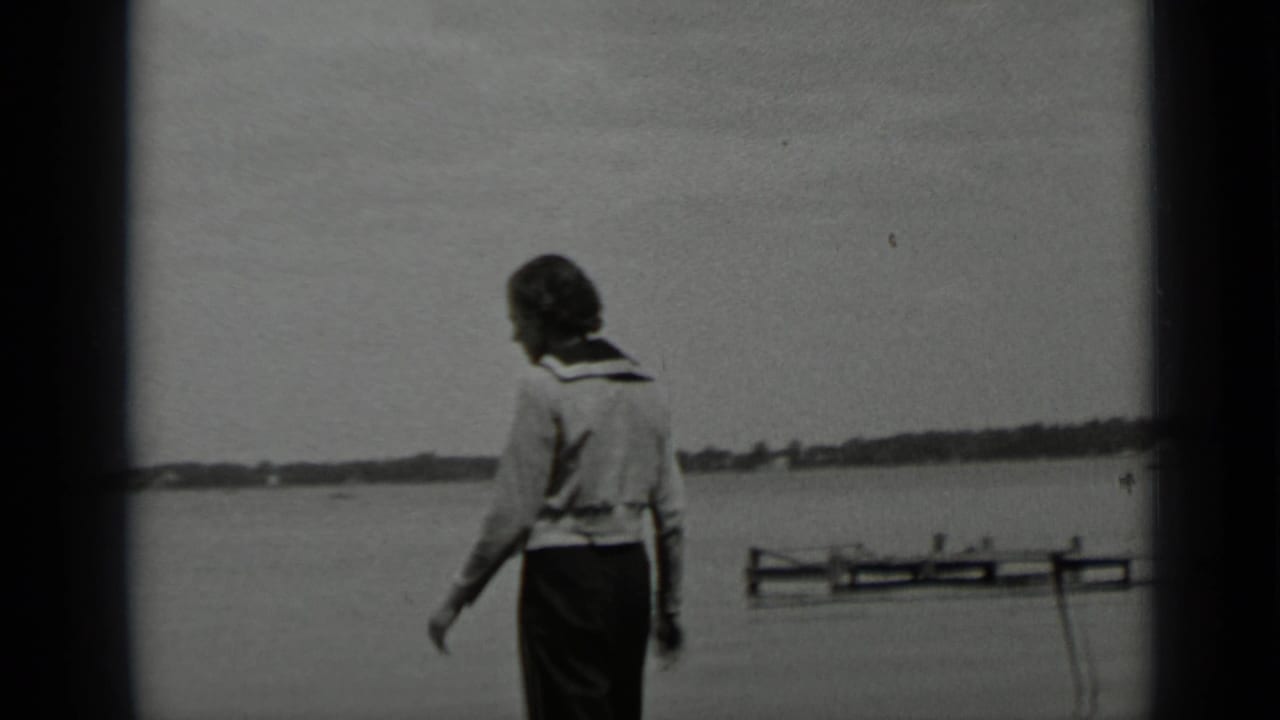 Woman seen from behind walking along a lakeshore with a small dock nearby.