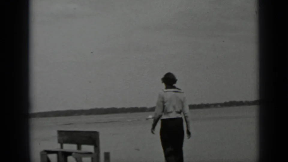 A woman walks along the Clear Lake shore, passing a bench-like structure or low dock element with open water and distant land behind her.