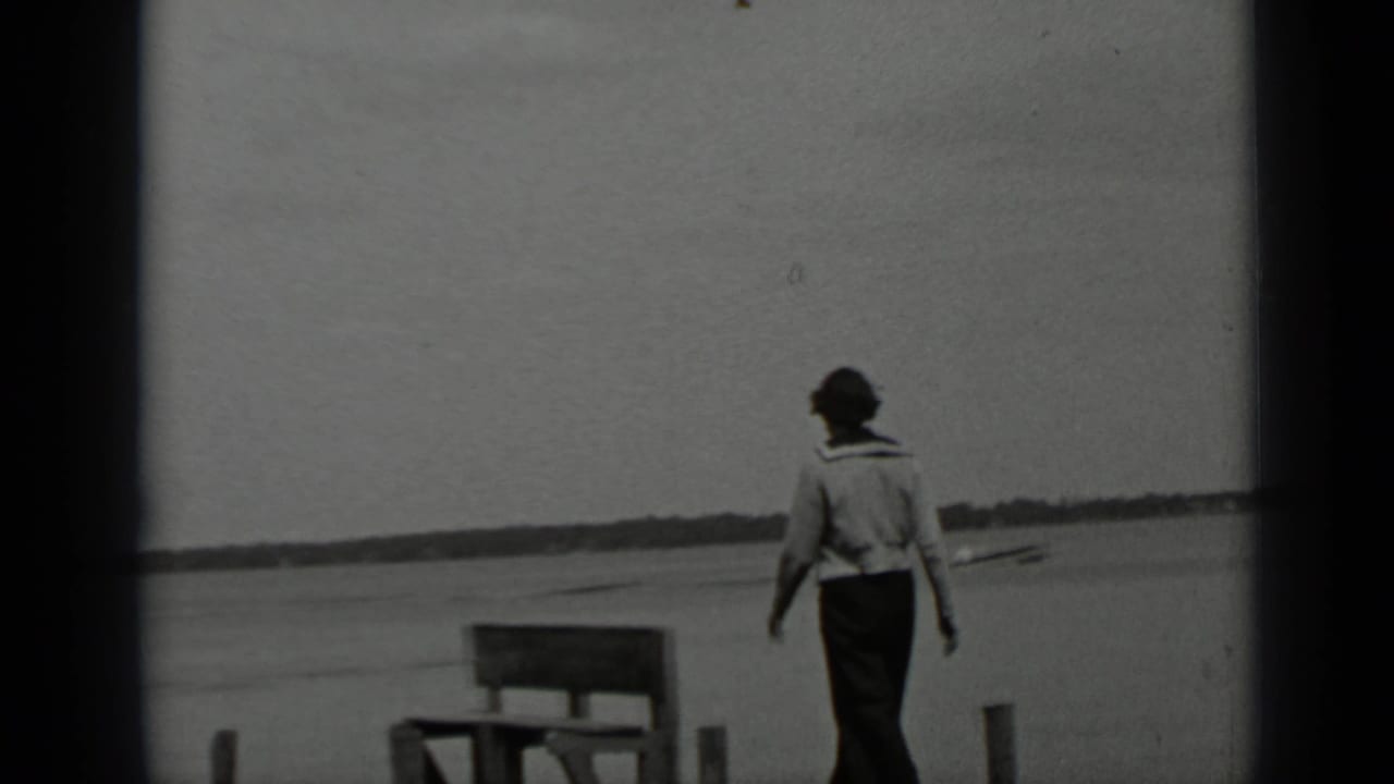 A woman in trousers walks away along a wooden pier at Clear Lake, California, with still water and distant shoreline behind her.