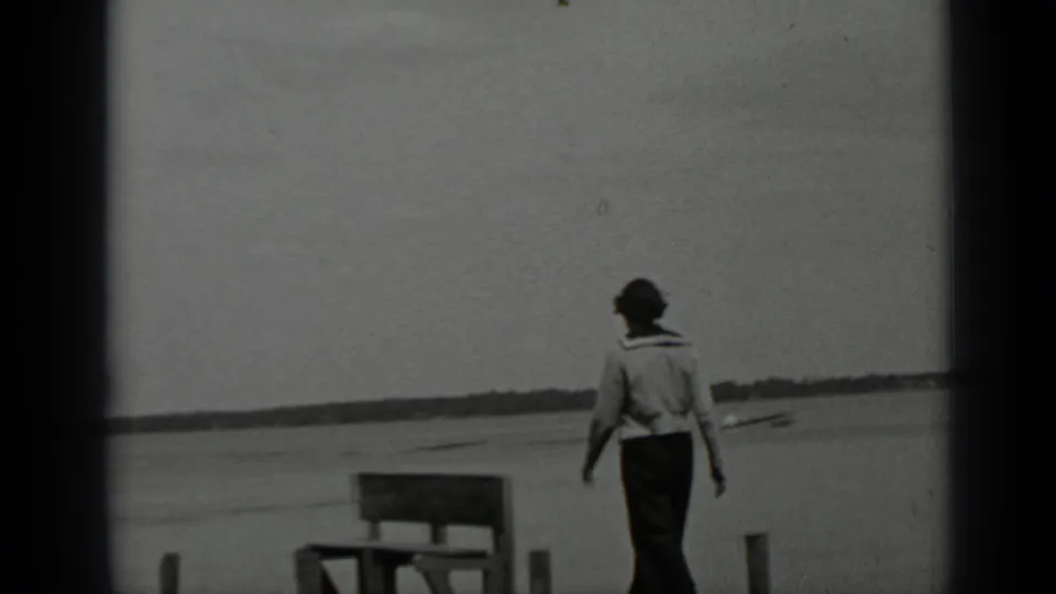 A woman in trousers walks away along a wooden pier at Clear Lake, California, with still water and distant shoreline behind her.
