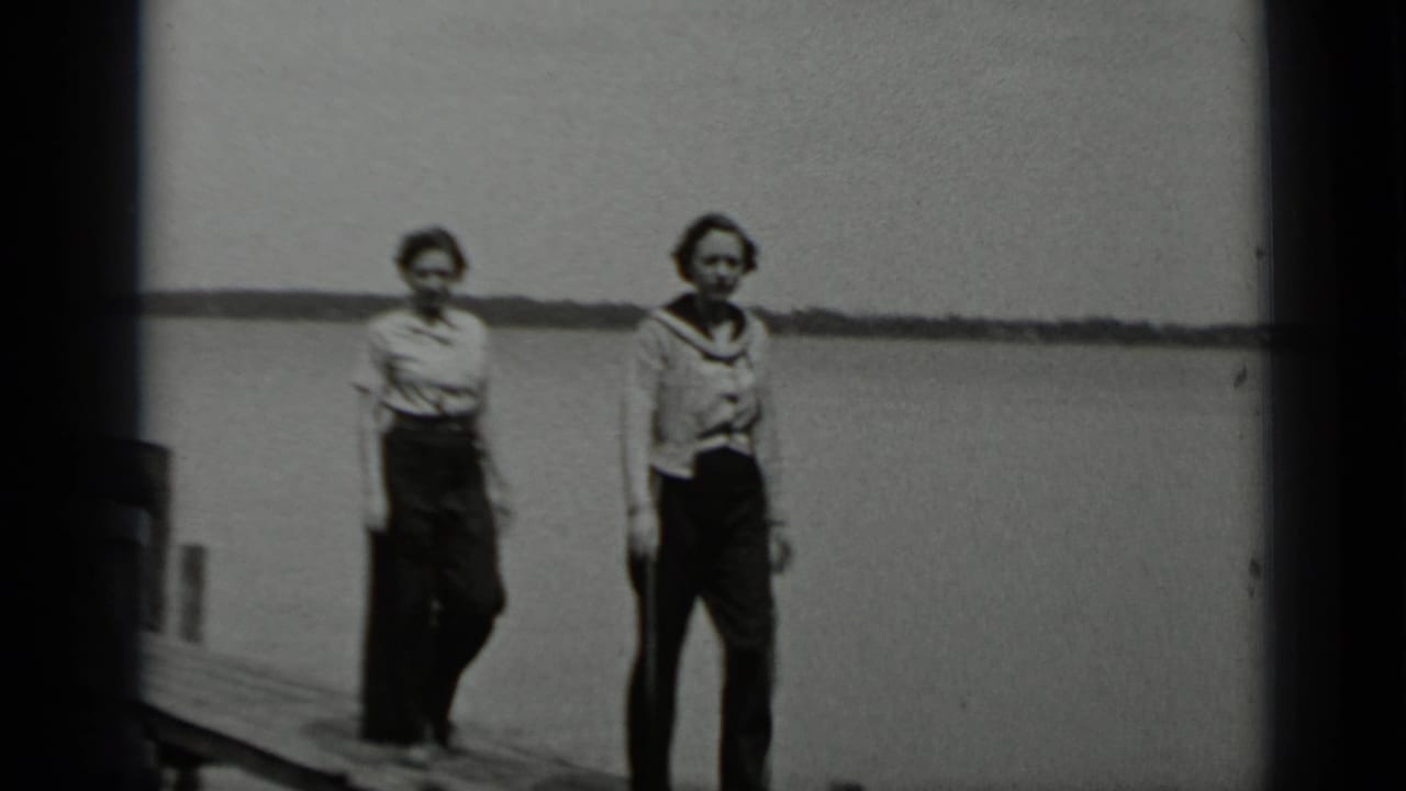 Two women in period clothing on a wooden pier at Clear Lake, California, with calm water and a low shoreline behind them.