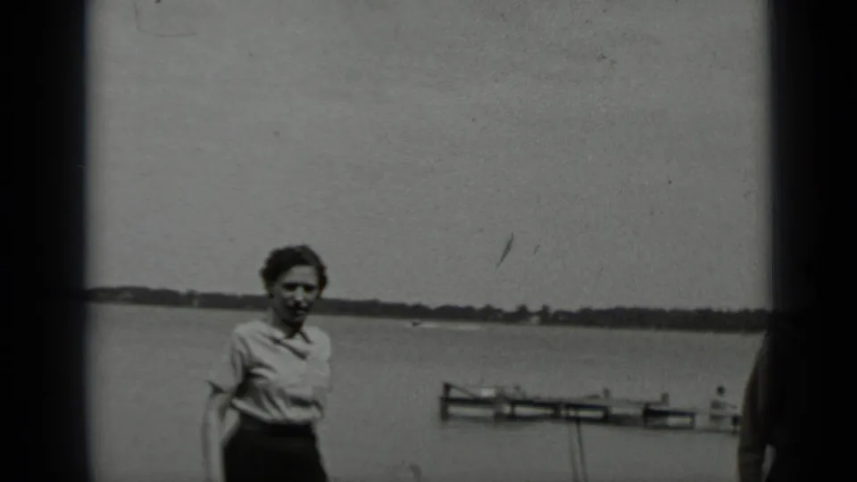 One woman stands or walks near the camera at Clear Lake, with small boats and the distant shoreline visible behind her.