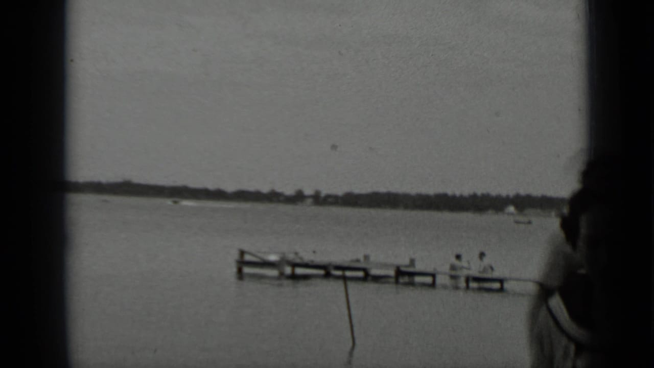 Lake and wooden pier with seated people, with part of a person at the right edge.